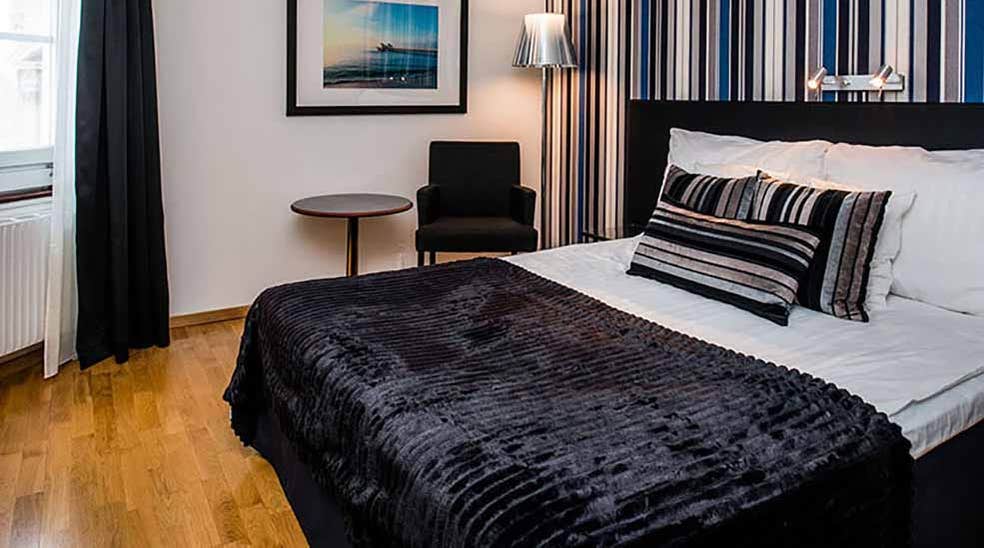 Standard dubbelrum med dubbelsäng, bord och fåtölj samt randig tapet på Quality Hotel Statt i Hudiksvall